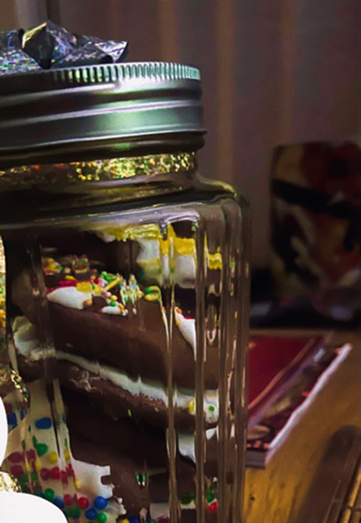 A close-up of a jar containing chocolate biscuits. The jar is decorated with sparkling gold and silver ribbon.