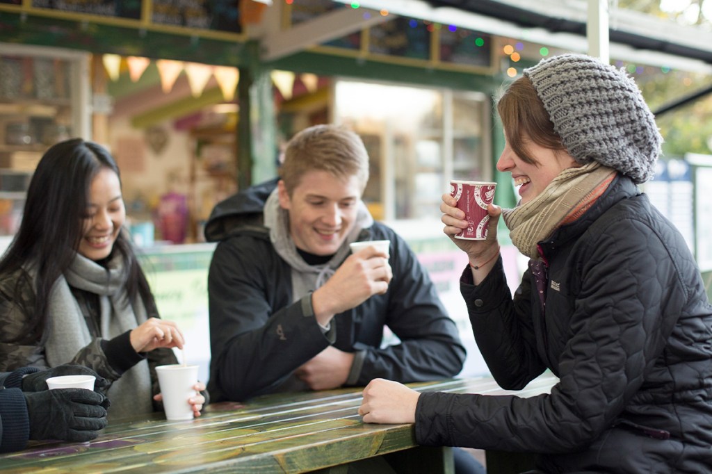 Three students at a picnic bench, drinking hot drinks.